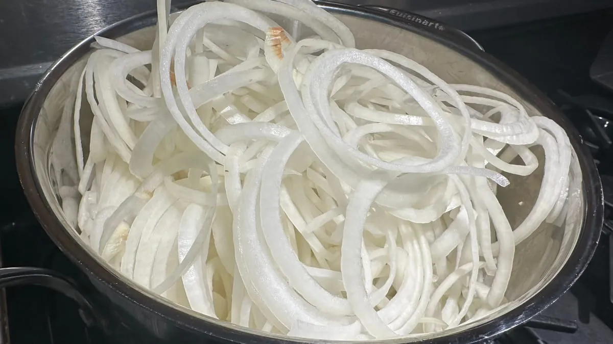 Paper-thin sweet onion rings from a mandoline, filling a stainless bowl