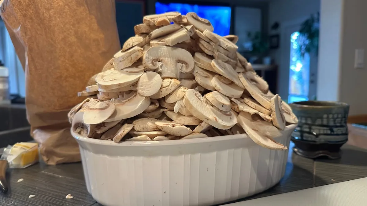 Two pounds of sliced white mushrooms heaped well past the rim of a white casserole dish